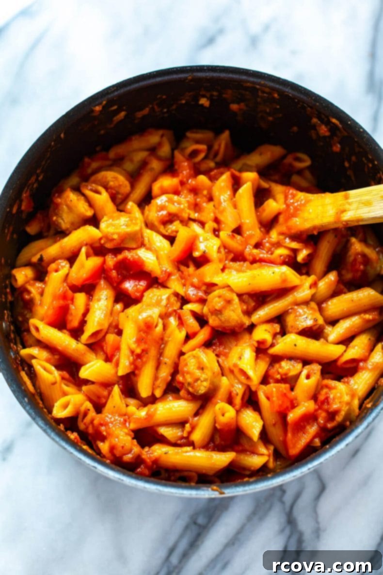 Experience the simplicity and flavor of this One-Pot Spicy Penne Arrabiata, a quick and healthy pasta meal with spicy tomato sauce, lean protein, and colorful bell peppers, perfect for busy evenings. A large pot of One-Pot Spicy Penne Arrabiata cooking on the stove, showing the pasta simmering in the rich tomato sauce with sausage and bell peppers.