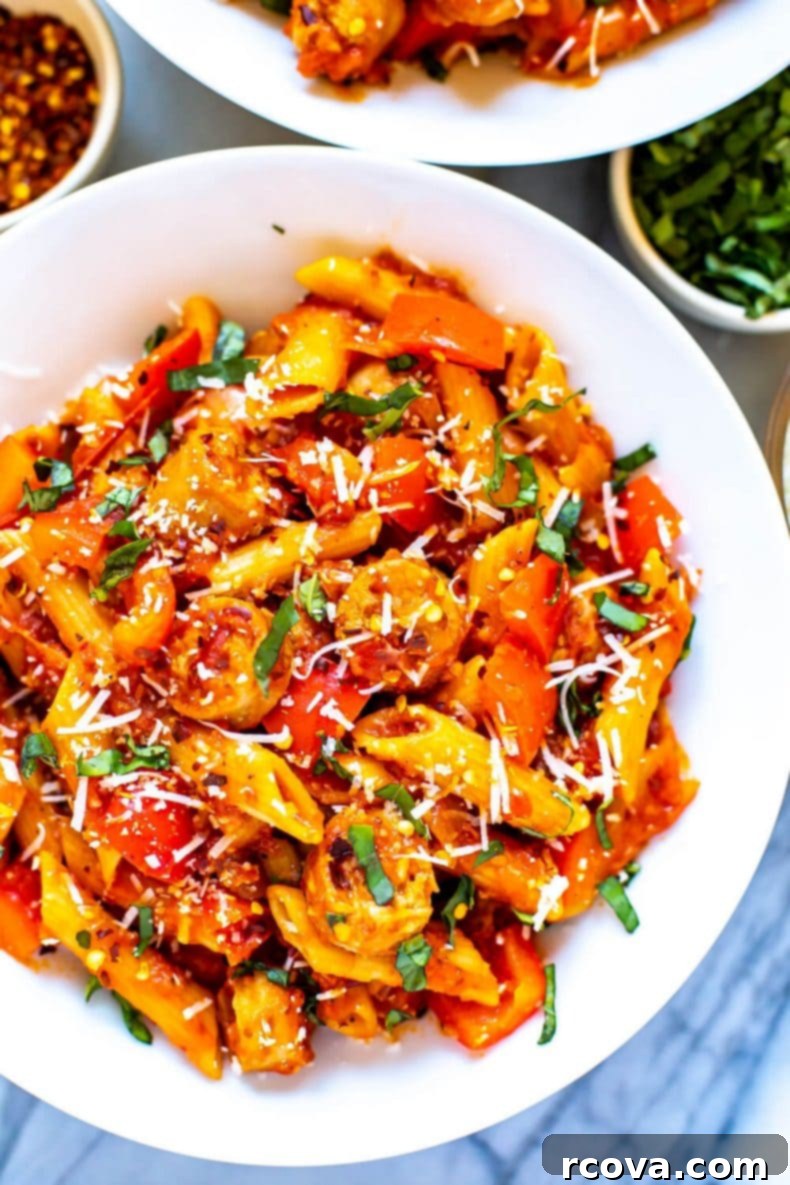 Enjoy a comforting bowl of Arrabiata pasta, a quick and healthy one-pot recipe featuring a spicy tomato sauce with bell peppers and sausage, ideal for any night of the week. Overhead shot of a delicious Arrabiata pasta dinner in a rustic bowl, garnished with green herbs, highlighting the rich texture of the spicy tomato sauce.