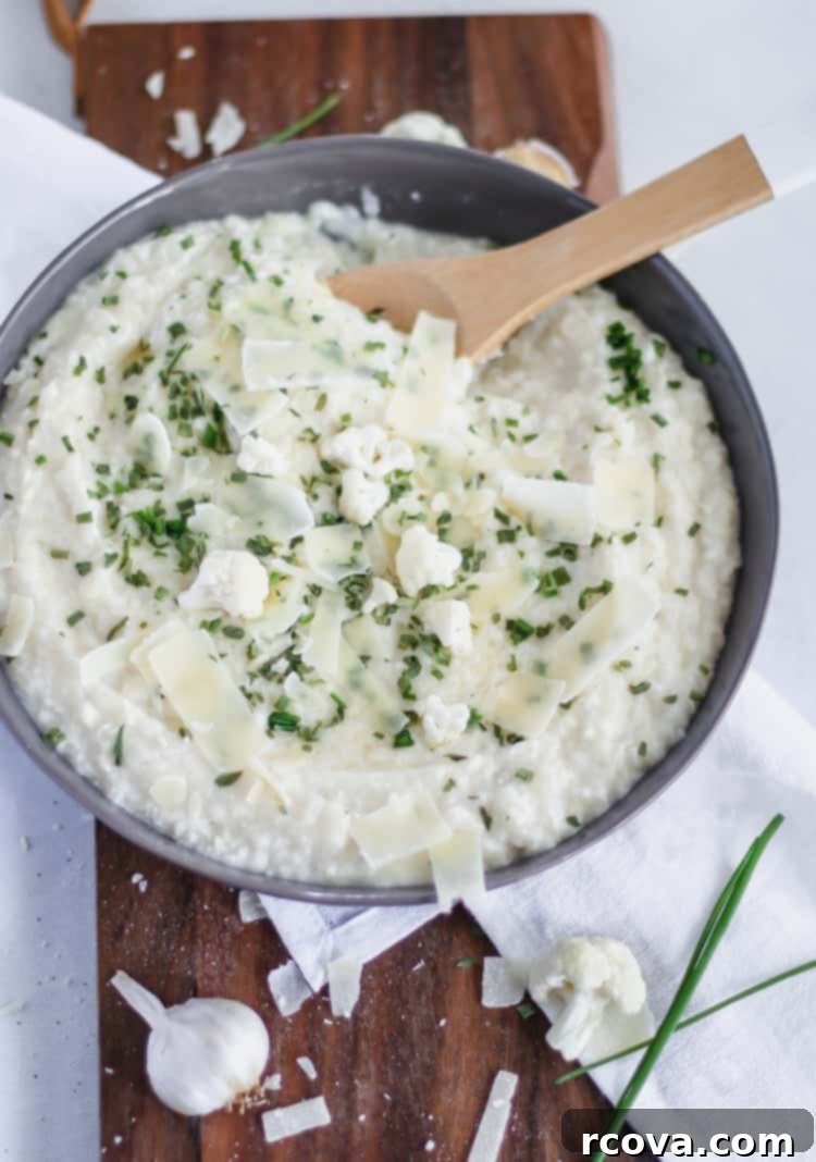 Roasted Garlic Parmesan Cauliflower Cloud 4 Bowl of creamy mashed cauliflower topped with roasted garlic cloves and shaved parmesan cheese, ready to be served.