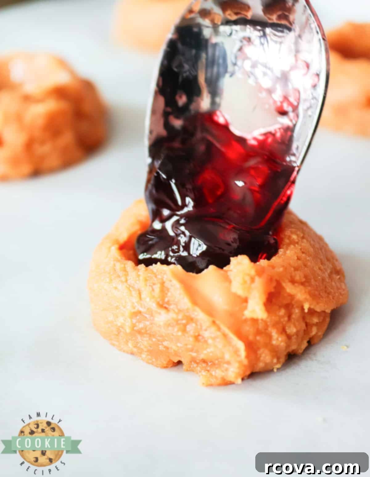 Peanut Butter Jelly Cookie Dreams 8 A teaspoon carefully adding a spoonful of vibrant red jelly into the indentation of a peanut butter cookie dough ball.