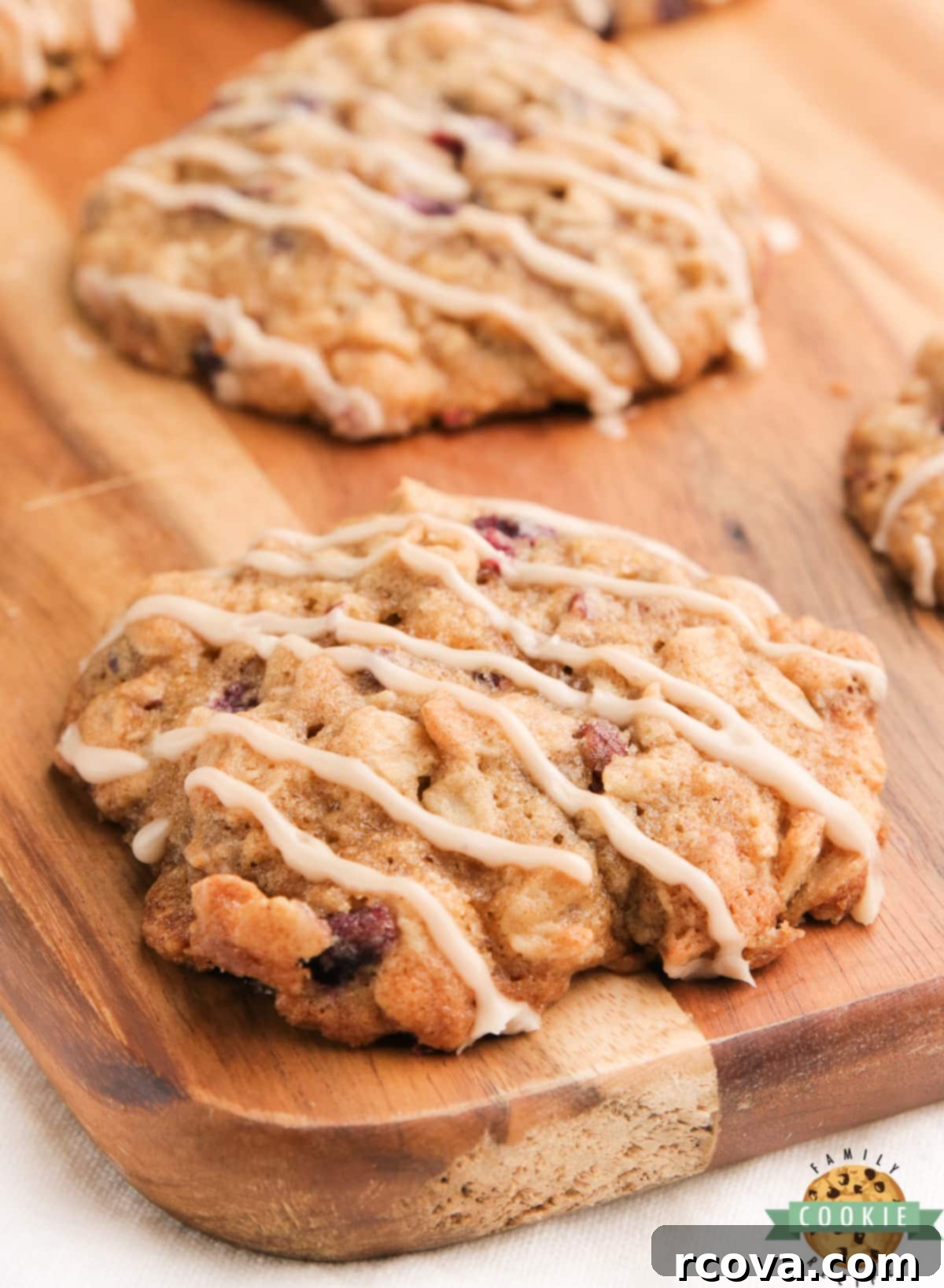 Ruby Glazed Pomegranate Oat Treats 9 A stack of three glazed pomegranate oatmeal cookies on a wooden board, with a close-up on their soft texture.