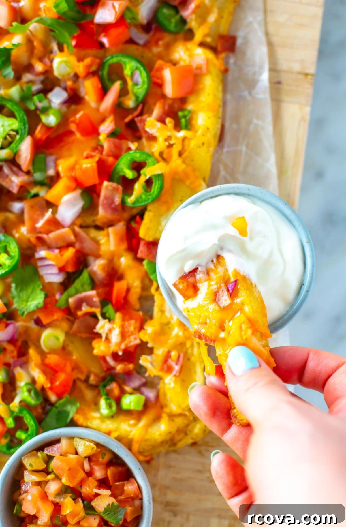 Hearty Irish Pub Nachos 8 A close-up of a hand delicately picking up a loaded Irish nacho from a serving platter, poised to dip it into a creamy swirl of sour cream.