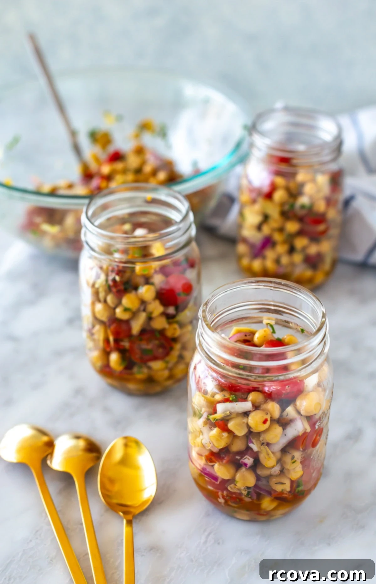 Effortless Mediterranean Chickpea Salad 8 Three mason jars being filled with Mediterranean chickpea salad, showcasing the layering process for meal prep.