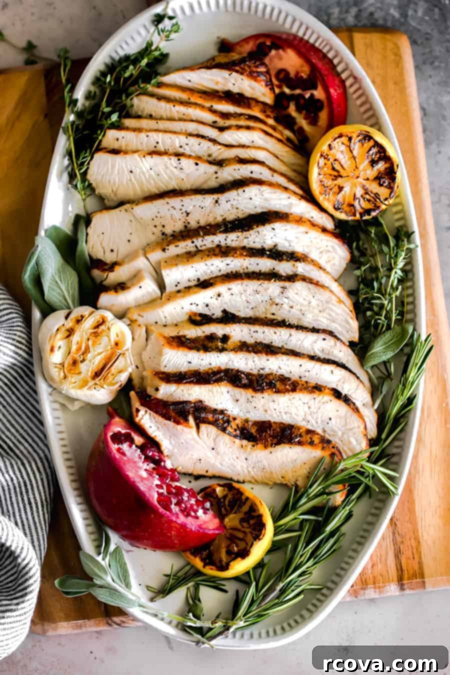 Perfect Air Fryer Turkey Breast 2 slices of turkey decoratively displayed on an oval serving tray with a garlic head, charred lemon and fresh sage, thyme and rosemary.