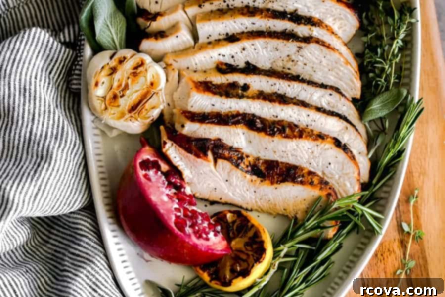 Perfect Air Fryer Turkey Breast 5 slices of turkey decoratively displayed on an oval serving tray with a garlic head, charred lemon and fresh sage, thyme and rosemary.
