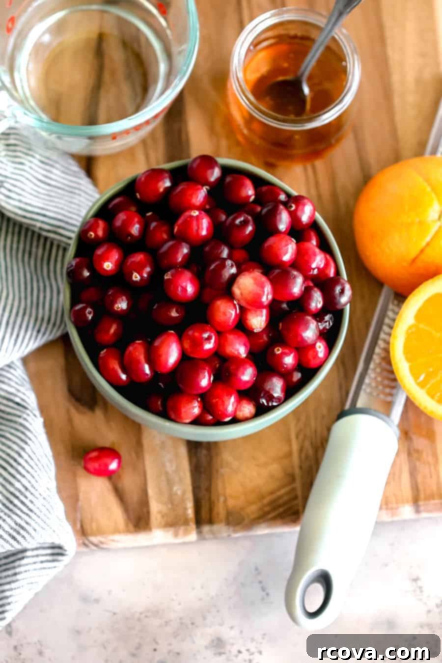 Honey-Kissed Orange Cranberry Sauce 3 Key ingredients for homemade cranberry sauce: a bag of fresh cranberries, honey, a navel orange, and water, with a lemon zester visible.