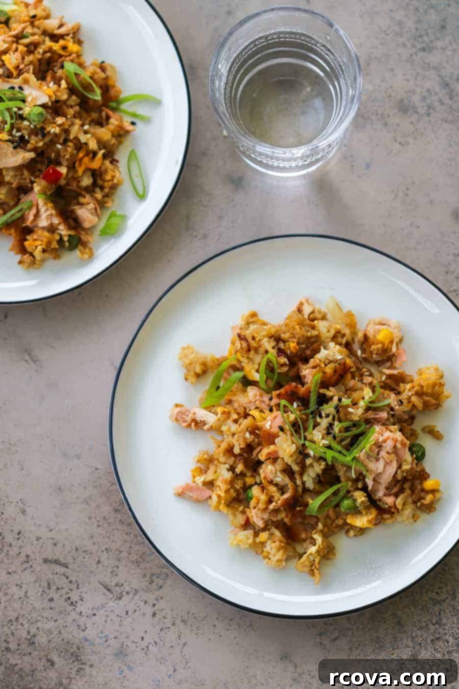 Effortless One-Pan Salmon Fried Rice 2 Close-up of fluffy salmon fried rice with peas, carrots, and cauliflower on a white plate, garnished with green onions.