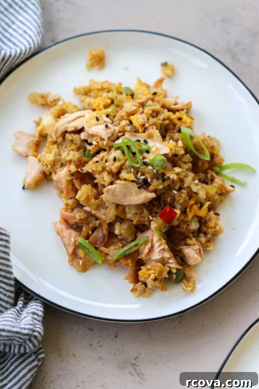 Effortless One-Pan Salmon Fried Rice 5 Overhead shot of a person mixing salmon, eggs, and vegetables in a skillet for fried rice.