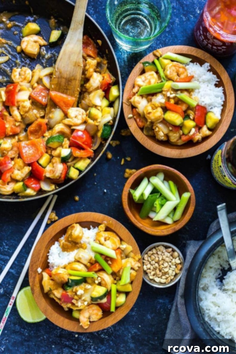 This 30-Minute Kung Pao Shrimp is a delicious, quick and easy stir fry that's perfect for getting dinner on the table quickly! Switch up the veggies to use whatever's leftover in your fridge! A sizzling skillet filled with spicy Chinese shrimp stir-fry, alongside two bowls ready for serving, highlighting the rich sauce and fresh ingredients.