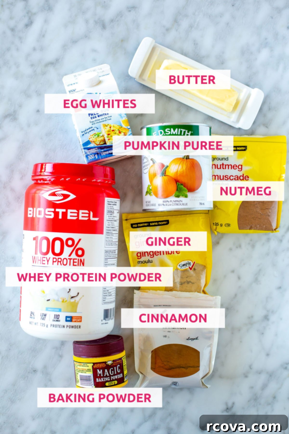 Easy 5-Ingredient Pumpkin Protein Pancakes 4 Ingredients laid out for pumpkin protein pancakes: a bowl of whey protein powder, a can of pumpkin puree, a stick of butter, a bowl of egg whites, a measuring spoon with baking powder, and a small dish of pumpkin spice blend.