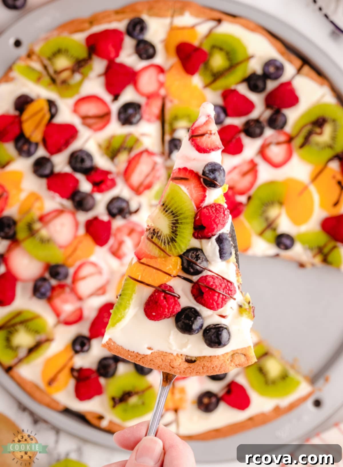 Giant Chocolate Chip Cookie Fruit Pizza 9 A hand reaching for a slice of colorful chocolate chip cookie pizza, indicating it's ready to be served and enjoyed.
