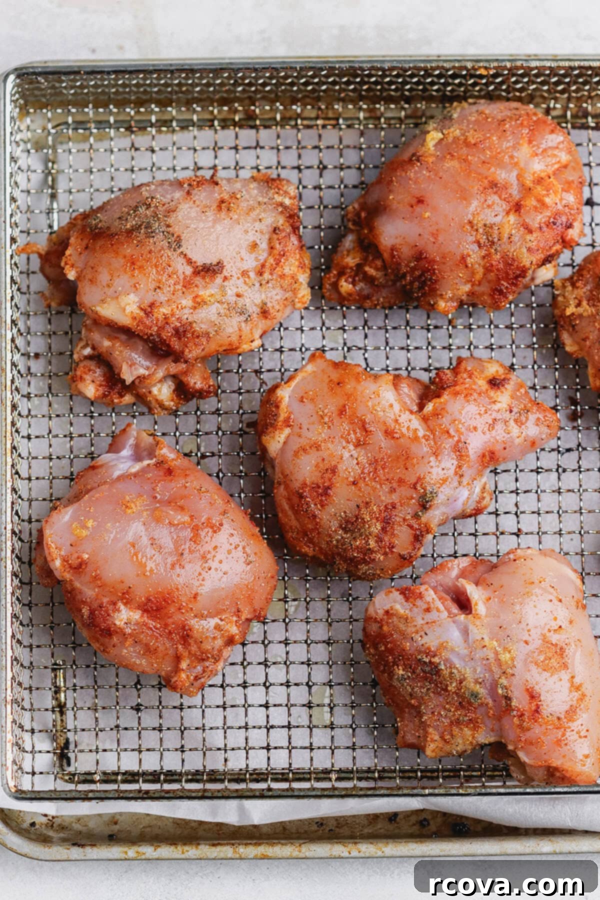 Crispy Air Fryer Chicken Thighs 4 Seasoned boneless skinless chicken thighs arranged on a metal air fryer basket, ready to cook.