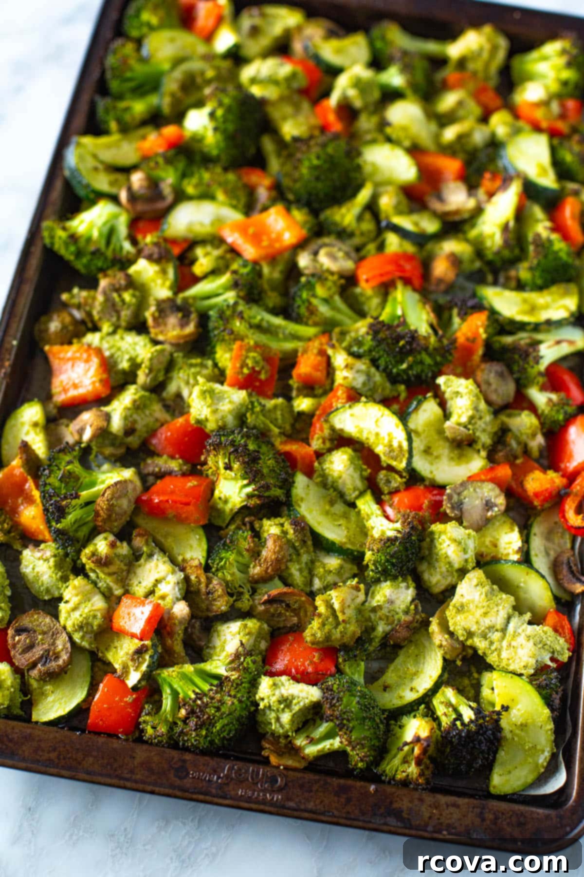 One-Pan Pesto Chicken Dinner 6 Close-up of baked sheet pan pesto chicken, showcasing tender chicken pieces and roasted vegetables like broccoli, bell pepper, and mushrooms, coated in vibrant pesto.