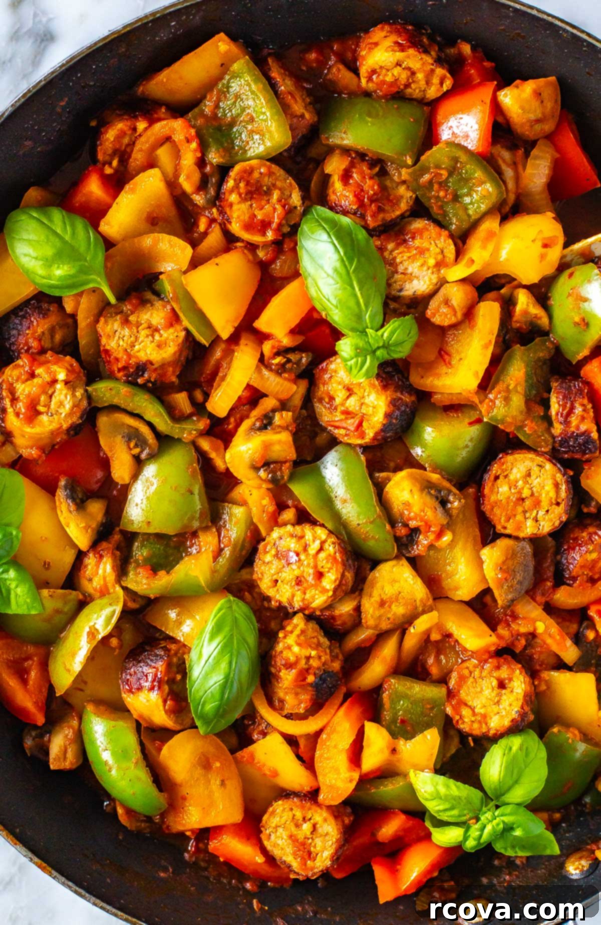 One-Pan Sausage, Peppers and Onions 8 A close-up shot of a steaming skillet filled with a vibrant mix of sausage, colorful bell peppers, and tender onions coated in a rich tomato sauce, garnished with fresh herbs.