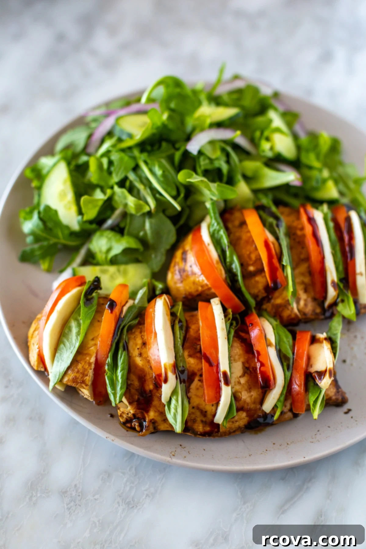Caprese Hasselback Chicken Bake 7 Close-up of baked Hasselback Caprese Chicken, revealing the stuffed layers of mozzarella, tomato, and basil, served with a fresh salad.