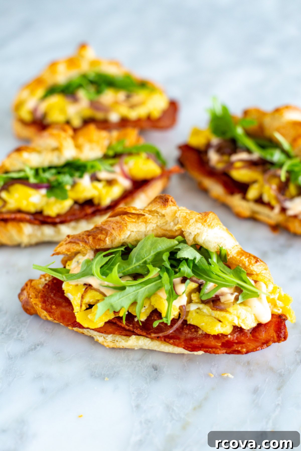 Fuel Your Mornings: Healthy Breakfast Prep 31 Four croissant breakfast sandwiches with bacon, scrambled eggs and arugula inside them.