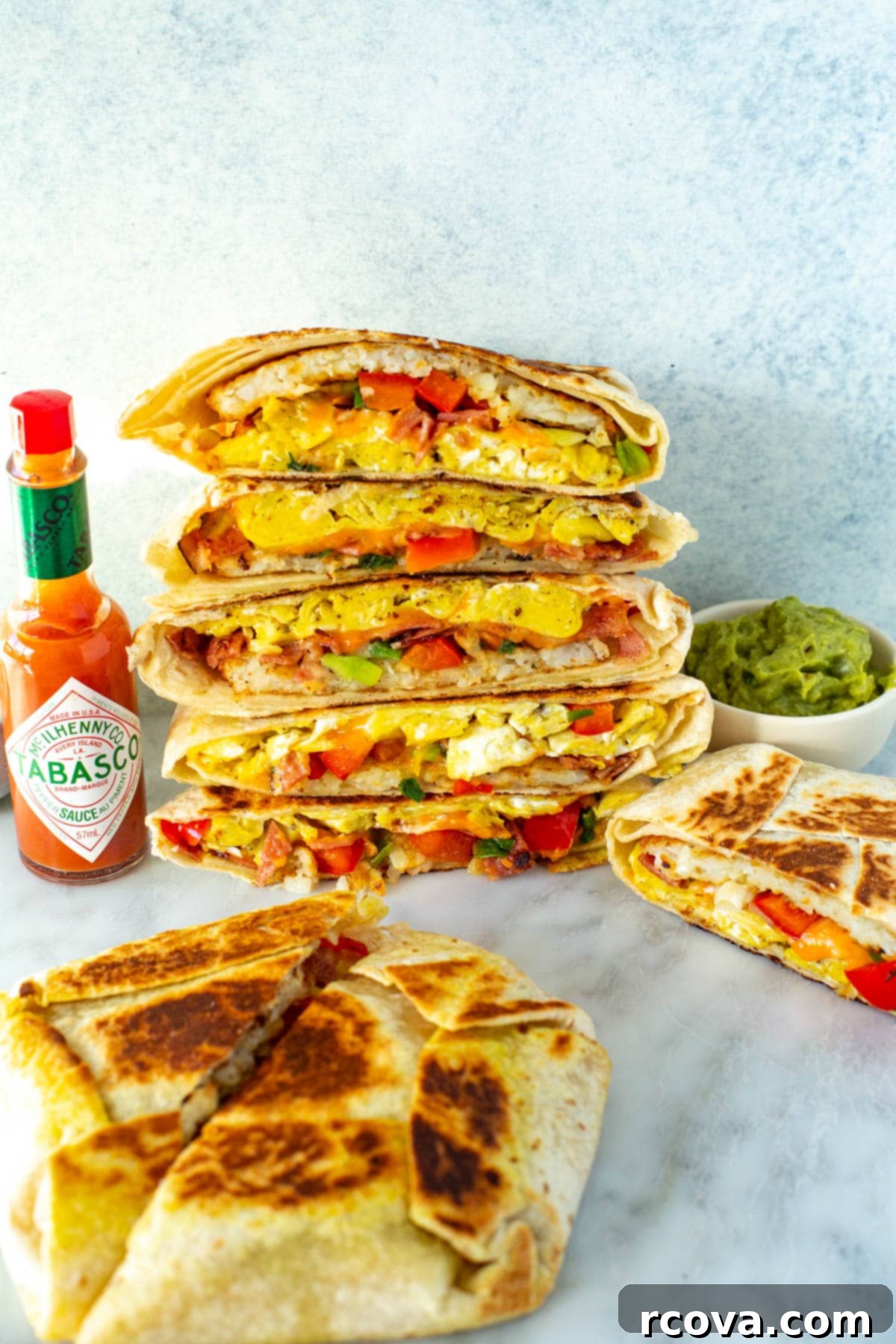 Fuel Your Mornings: Healthy Breakfast Prep 32 Cut open breakfast crunchwraps stacked together with a side of hot sauce and guacamole.