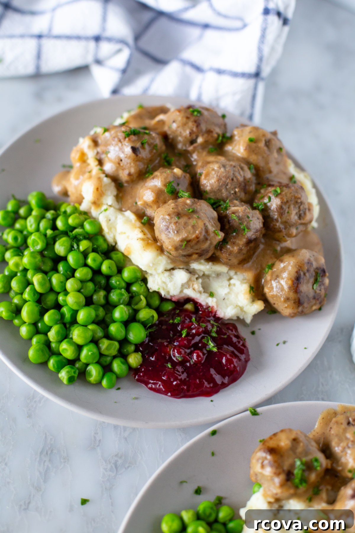 IKEA's Signature Meatballs Slow Cooked 9 Close-up of Swedish meatballs served with peas and a spoonful of red lingonberry jam.