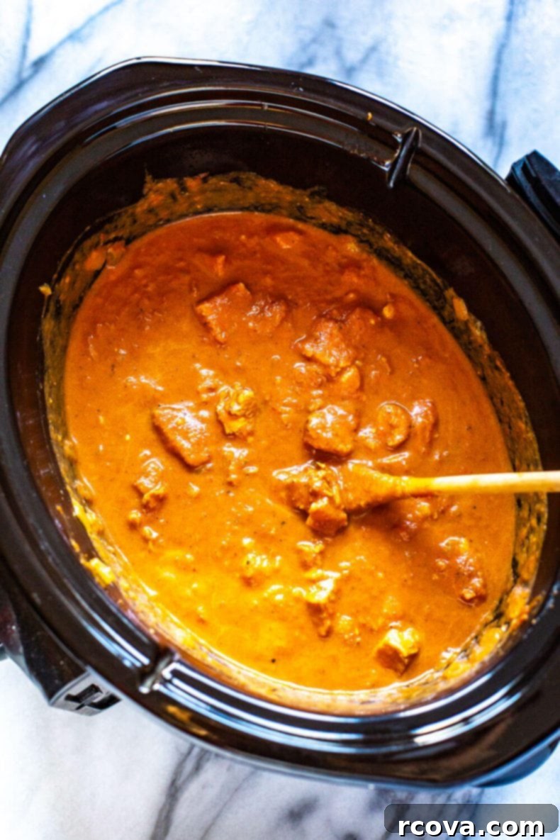 Slow Cooker Chicken Tikka Masala is a delicious, healthy way to enjoy Indian cuisine, and it cooks all day on low so you can enjoy a tasty curry after a long day without all the legwork! #slowcookerrecipes #chickentikkamasala Chicken Tikka Masala cooking in a slow cooker, showing the rich, vibrant sauce and tender chicken pieces