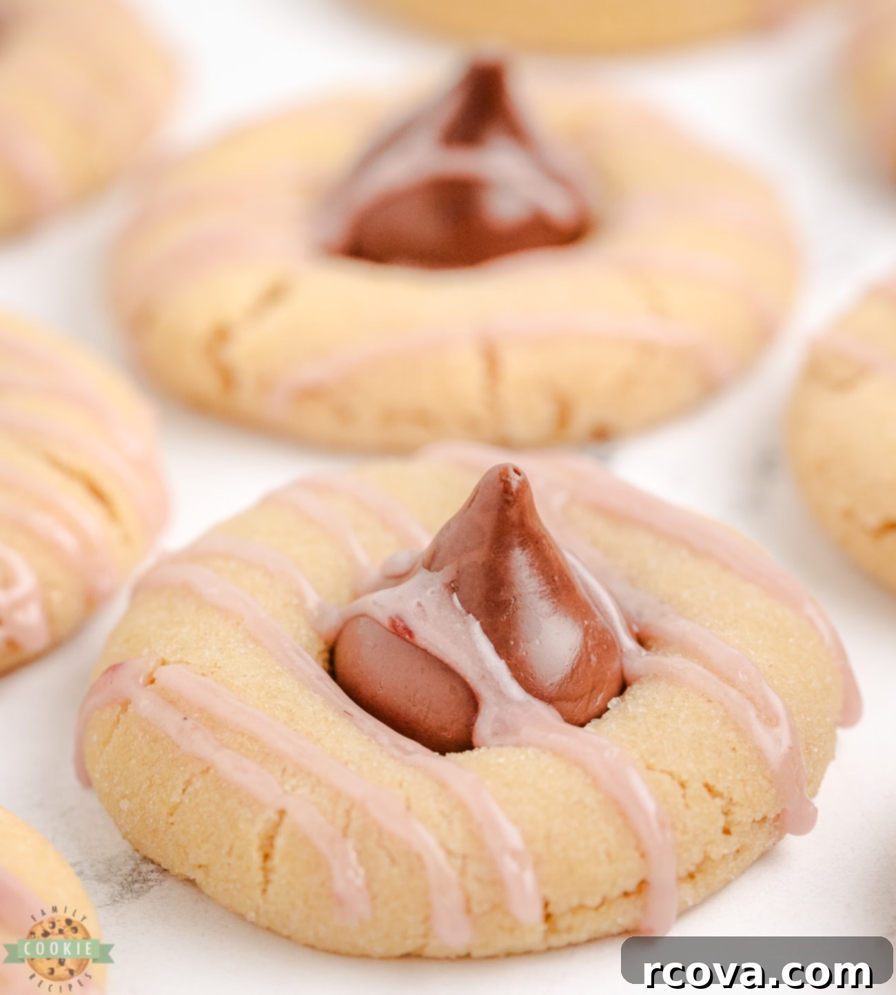 Luscious Raspberry Almond Kiss Cookies 3 Raspberry almond kiss cookies with a delicate pink drizzle on a white surface.
