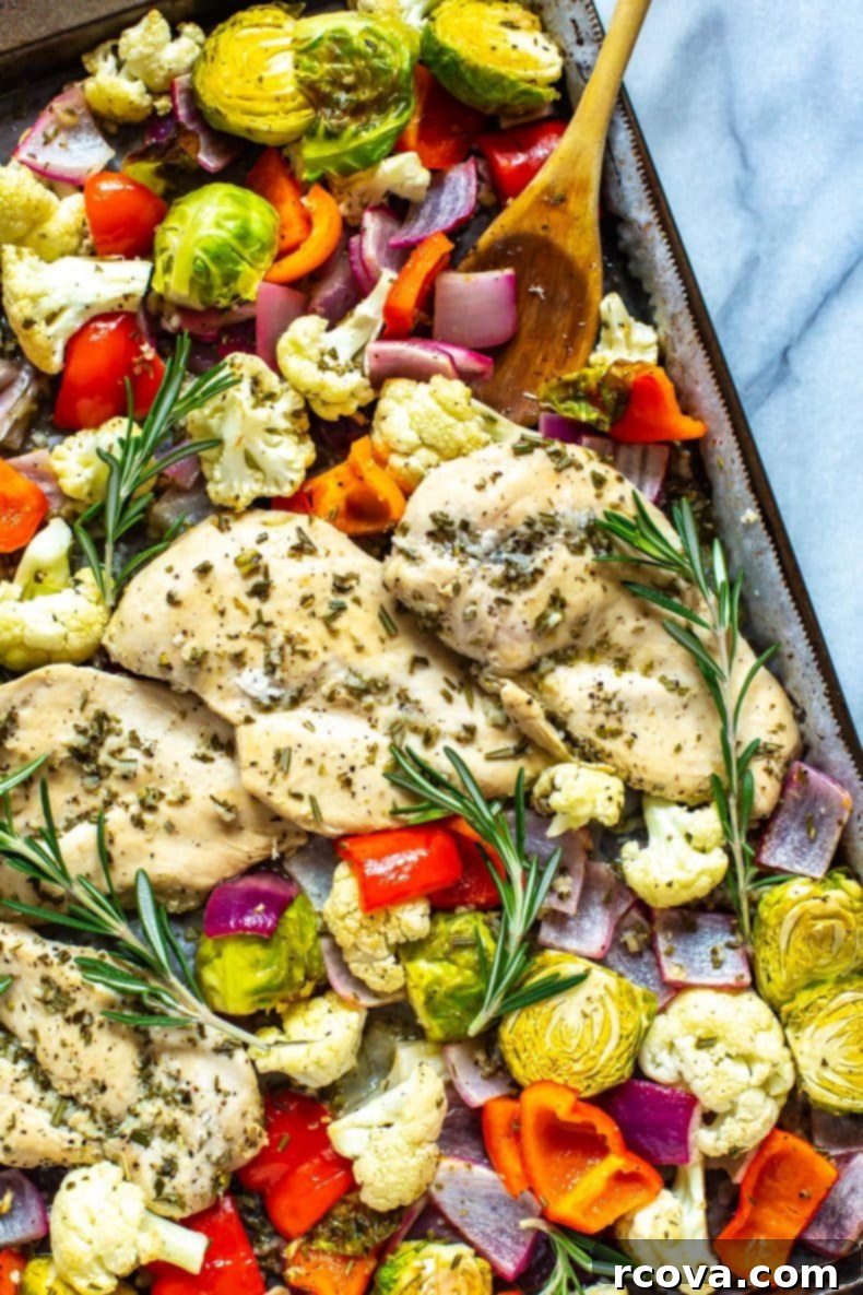 Our Sheet Pan Rosemary Chicken is a healthy, low-carb chicken meal prep recipe. It's perfect as a 30-minute dinner or to pack up as weekly lunch bowls!  A perfectly cooked Sheet Pan Rosemary Chicken dinner on a white plate, showcasing golden-brown chicken and caramelized vegetables like red peppers, brussels sprouts, and cauliflower.