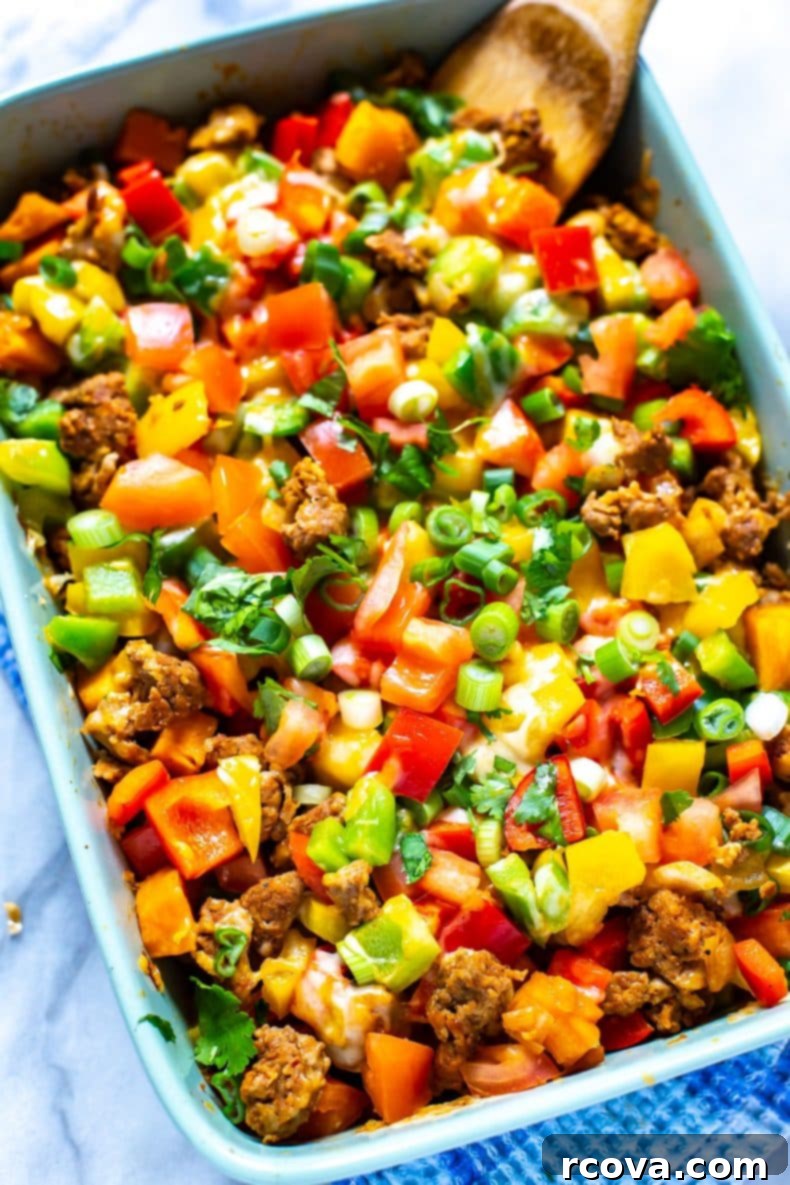 A vibrant and cheesy healthy ground turkey taco bake, rich with diced bell peppers, onions, tomatoes and melted cheddar cheese. Close-up of baked taco casserole with melted cheese, ground turkey, and fresh toppings.