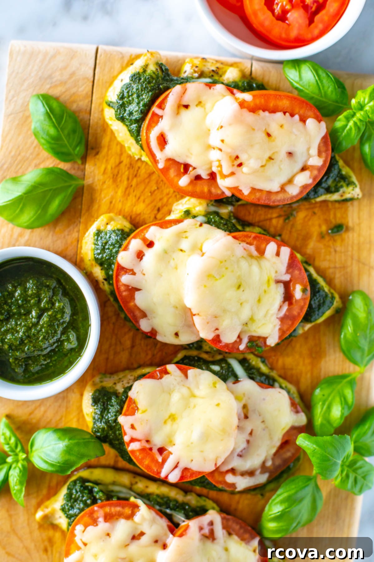 One-Pan Pesto Chicken Bake 8 Four chicken cutlets topped with pesto, tomato and mozzarella on a butcher block, highlighting the delicious topping.