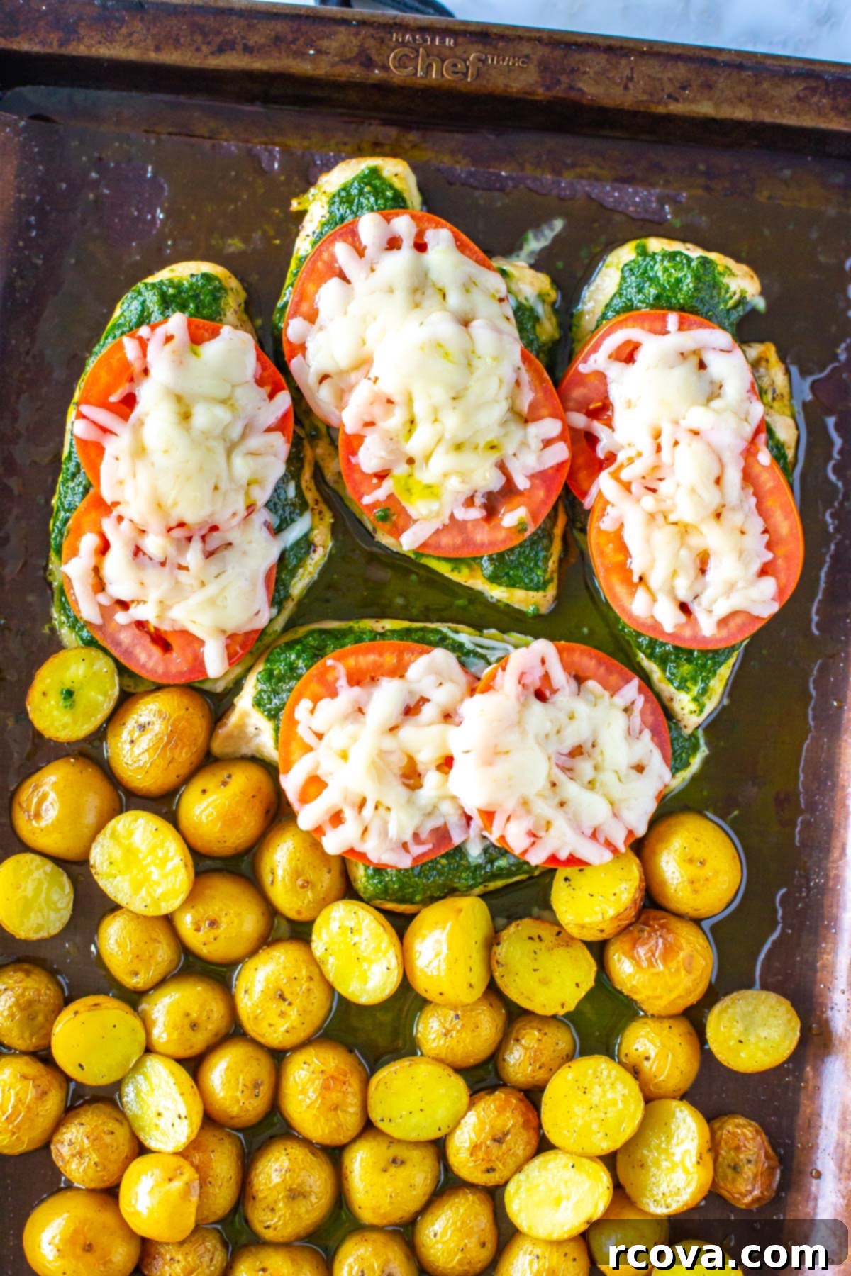 One-Pan Pesto Chicken Bake 9 Four chicken cutlets topped with pesto, tomato and mozzarella on a sheet pan with roasted potatoes, fresh out of the oven.