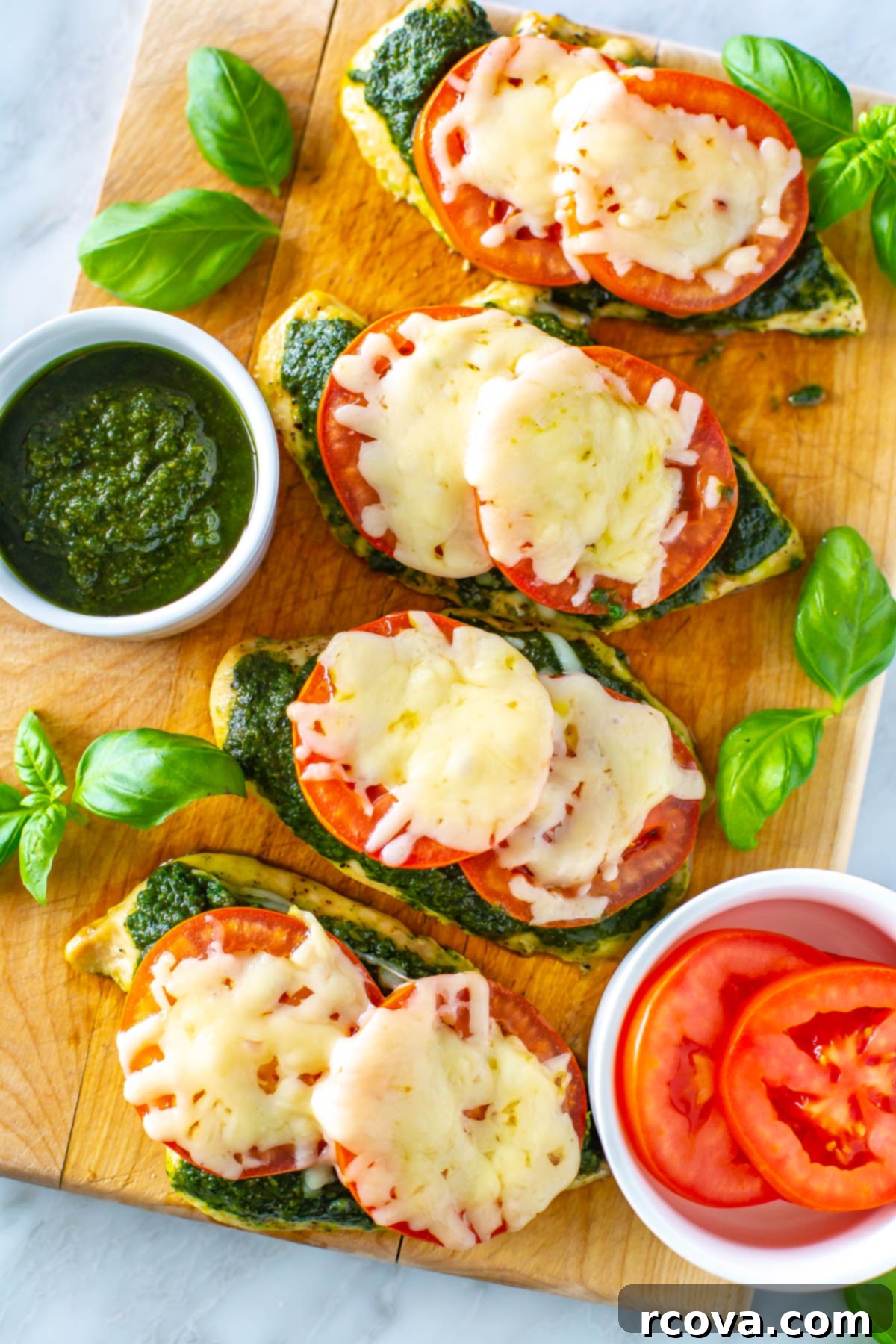 One-Pan Pesto Chicken Bake 10 Four chicken cutlets topped with pesto, tomato and mozzarella on a butcher block, showcasing the final appetizing dish.