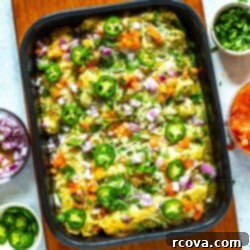 Savory Make-Ahead Chicken Enchiladas Verdes 6 Chicken enchiladas verdes in a black casserole dish garnished with sliced jalapeno, diced red onion, and cilantro.