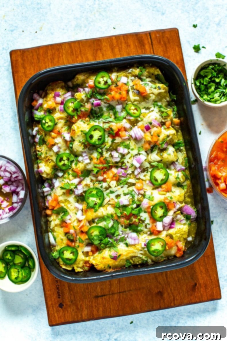 This Chicken Enchiladas Verdes recipe is made with tomatillo-based salsa verde and comes together as an easy dinner casserole - it also works great as flavorful meal prep lunches! #greenenchiladas #enchiladasverdes #chicken Pan of delicious green chicken enchiladas topped with sliced jalapeños and fresh cilantro, ready to be served.