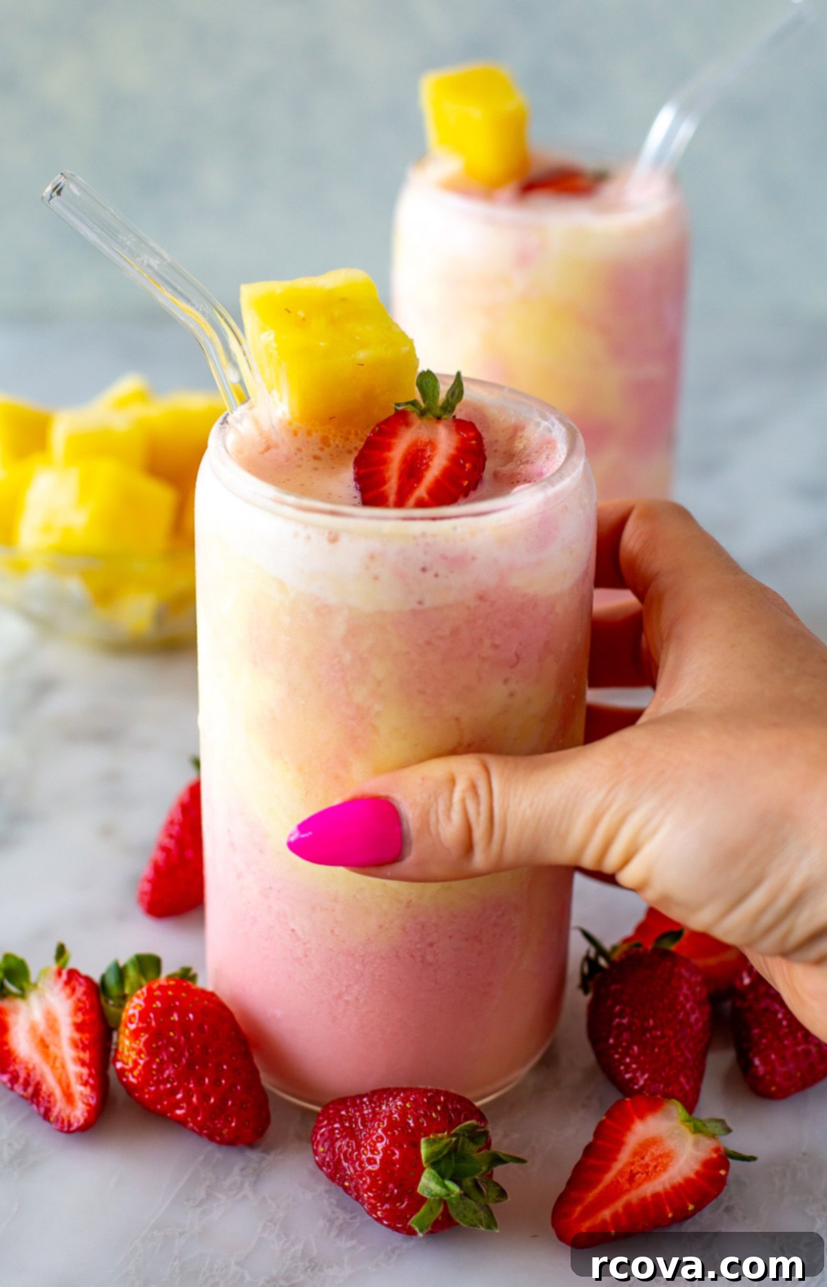 Power-Packed Protein Blends for Wellness 11 A side shot of a hand holding a glass of a layered strawberry and pineapple smoothie, a tropical and healthy blend.