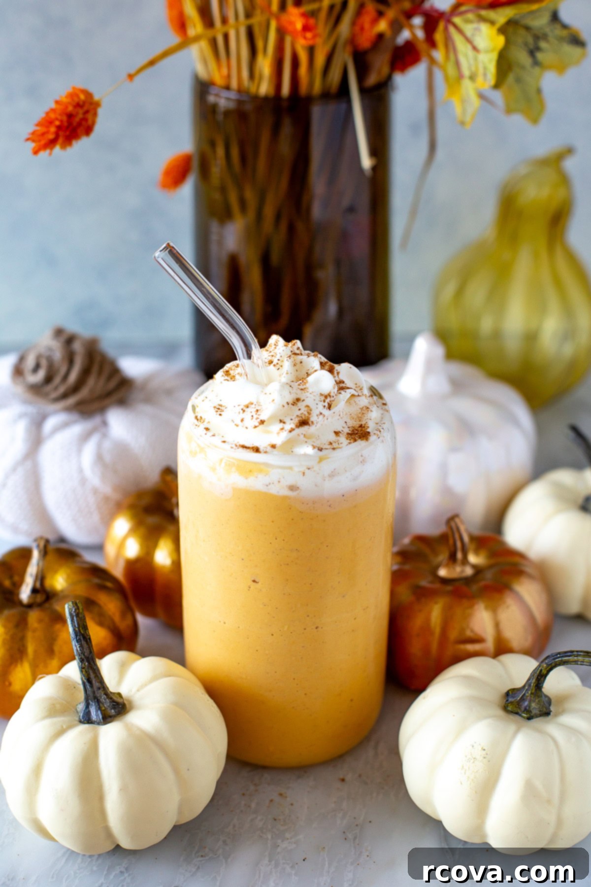 Power-Packed Protein Blends for Wellness 13 Side shot of a glass of pumpkin spice protein shake with whipped cream and a straw, surrounded by decorative pumpkins, a perfect fall treat.