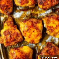 Succulent Baked Chicken Thighs with Crispy Skin 10 A close-up of seasoned baked chicken thighs on a sheet pan with prepared with parchment paper.