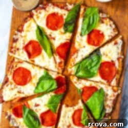 Ultimate 3-Ingredient Cauliflower Pizza Crust 10 Cauliflower Crust Pizza with pepperoni and basil, cut into slices on a cutting board. One slice has a bite taken out of it.