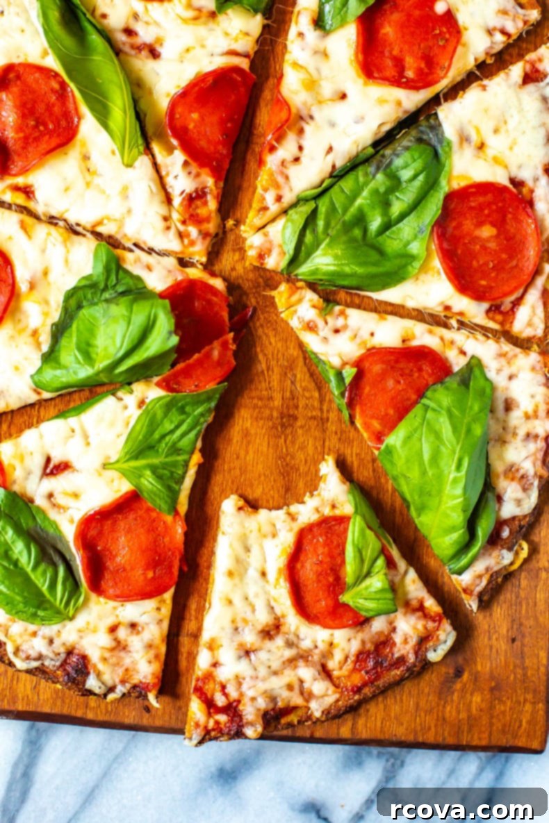 Ultimate 3-Ingredient Cauliflower Pizza Crust 8 A delicious Cauliflower Crust Pizza with pepperoni and basil, sliced on a wooden cutting board. A single slice is held up, showing the crispy texture.