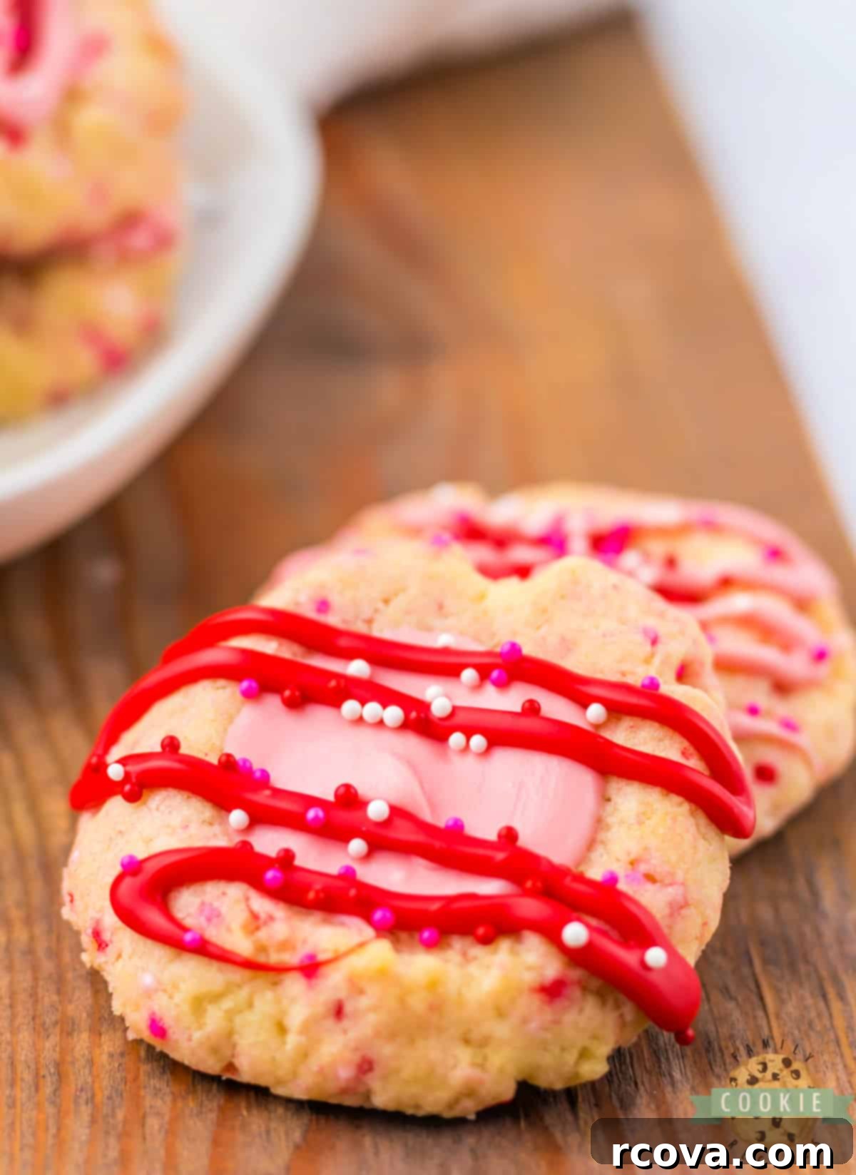 Valentines Thumbprint Cookies 14 Close-up of a buttery thumbprint cookie with pink chocolate filling and red chocolate drizzle, adorned with sprinkles.