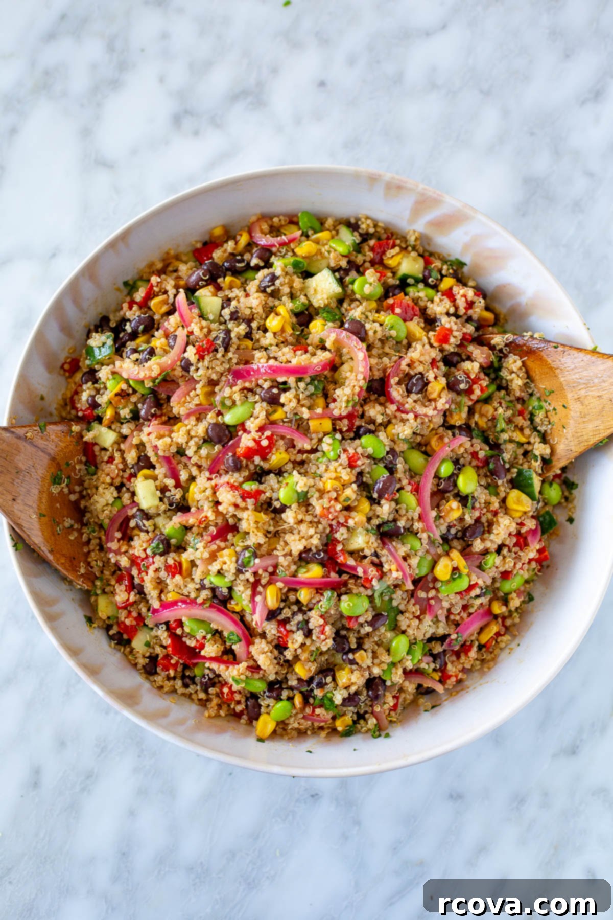 Speedy & Satisfying Quinoa Salad 8 Overhead shot of vibrant quinoa salad with two wooden spoons tossing the salad in a large white bowl