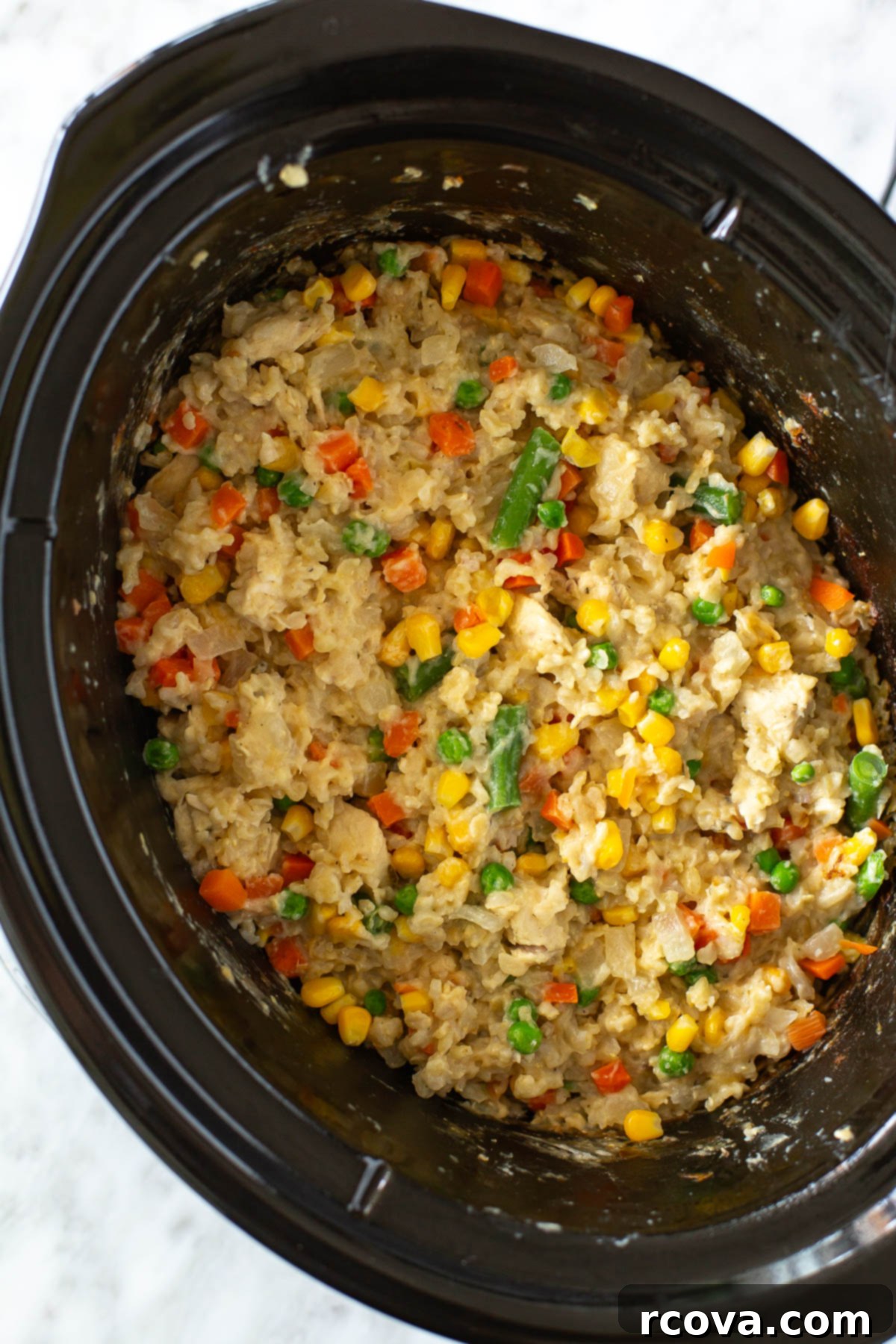 Effortless Slow Cooker Chicken and Rice 9 A close-up of creamy chicken and rice cooking in a red crockpot, showing its rich texture and steam.