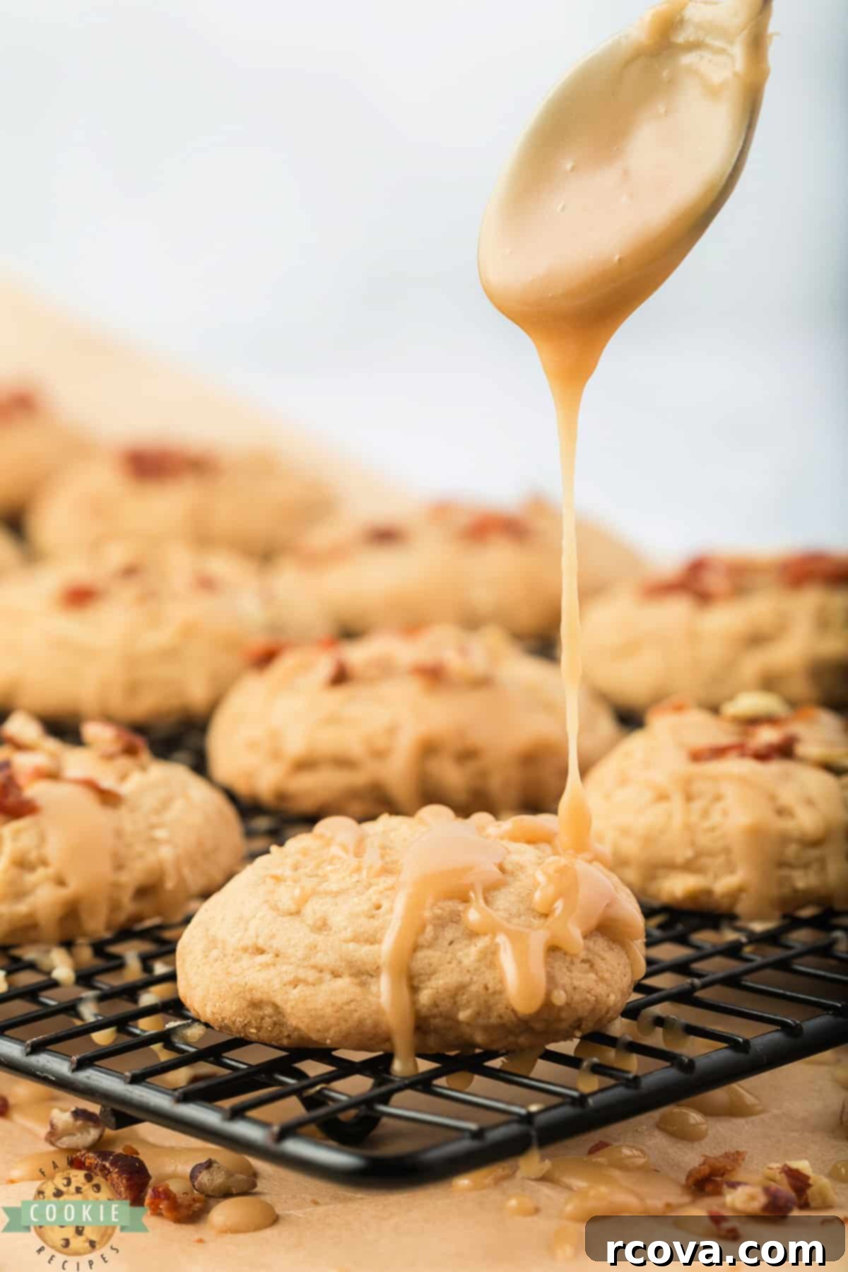 Sweet & Savory Maple Bacon Cookies 9 A hand drizzling a generous amount of maple glaze over baked maple bacon cookies on a cooling rack, preparing them for the final topping.