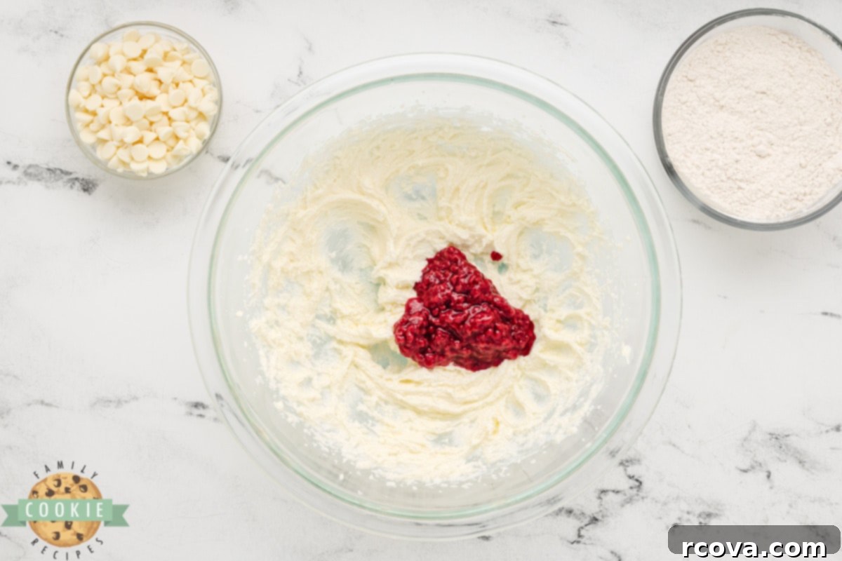 Ruby Red Raspberry Bites 7 Adding warm, mashed frozen raspberry mixture to the creamed butter and sugar in a bowl.