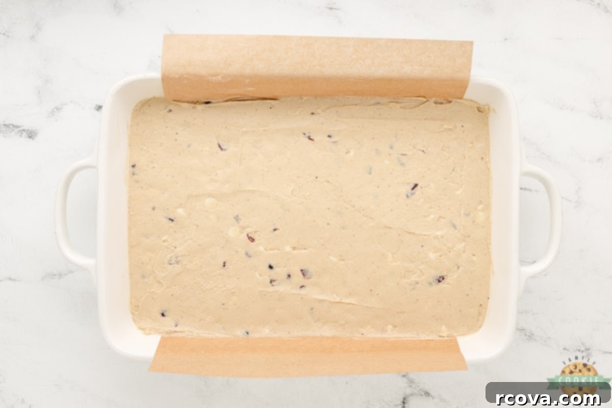 Irresistible White Chocolate Cranberry Cookie Bars 9 Spreading thick cookie dough evenly into a 9x13 inch baking pan lined with parchment paper for easy removal.