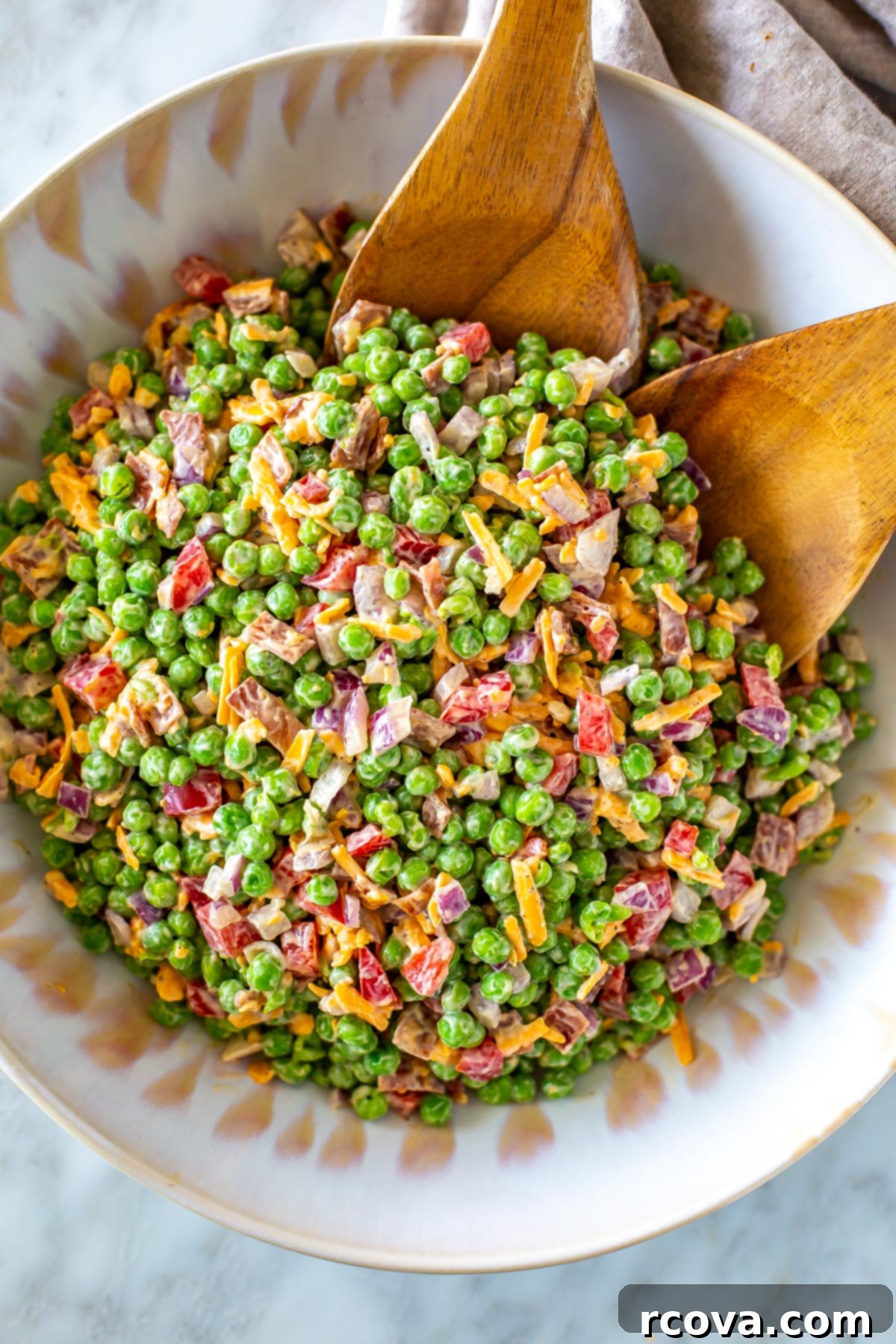 Over 25 Delicious No-Cook Recipes for Summer 12 Creamy pea salad in a large salad bowls with two wooden tongs in it.