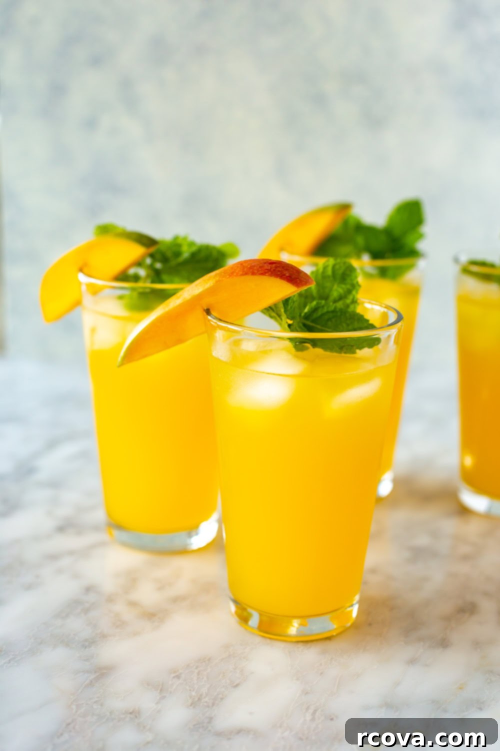 Summer's Coolest Sips 7 Two tall glasses of golden mango iced tea, garnished with fresh mango slices and mint sprigs.