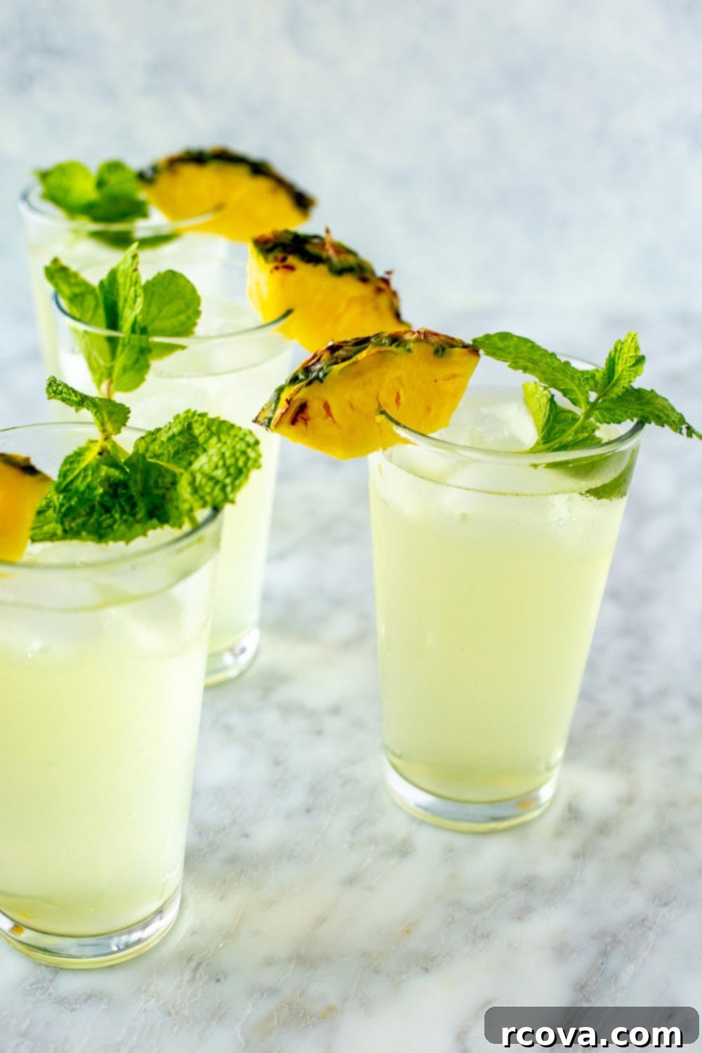 Summer's Coolest Sips 8 Tall glasses filled with frosty pineapple coconut coolers, garnished with fresh pineapple and mint.