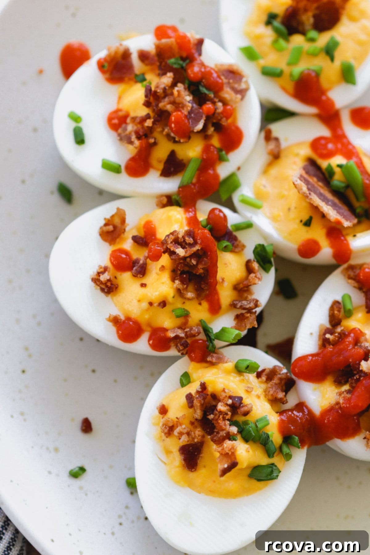 Fiery Sriracha Bacon Deviled Eggs 2 sriracha deviled eggs with bacon on a white plate