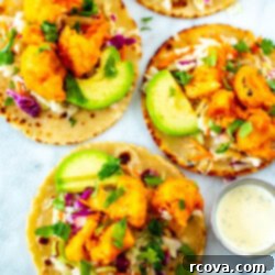 Zesty Buffalo Cauliflower Tacos 11 A close-up shot of four buffalo cauliflowe tacos topped with avocado slices with a side of ranch dressing.