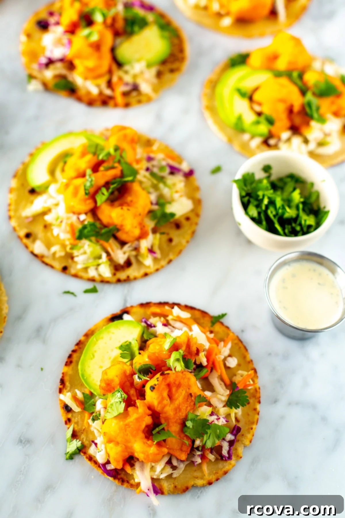 Zesty Buffalo Cauliflower Tacos 9 A close-up shot of several buffalo cauliflower tacos with little bowls of cilantro and ranch dressing on the side.