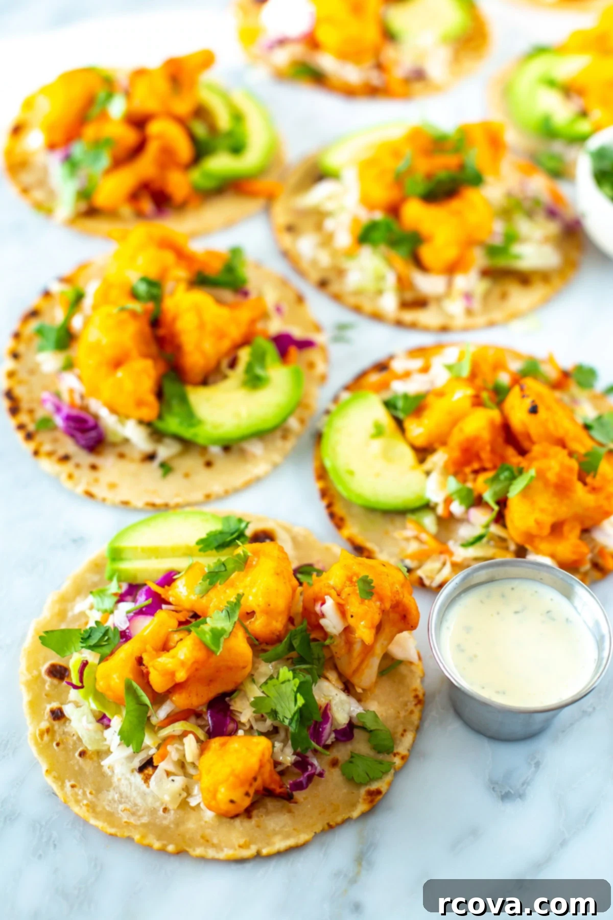 Zesty Buffalo Cauliflower Tacos 10 A shot of several buffalo cauliflower tacos with little bowls of cilantro and ranch dressing on the side.