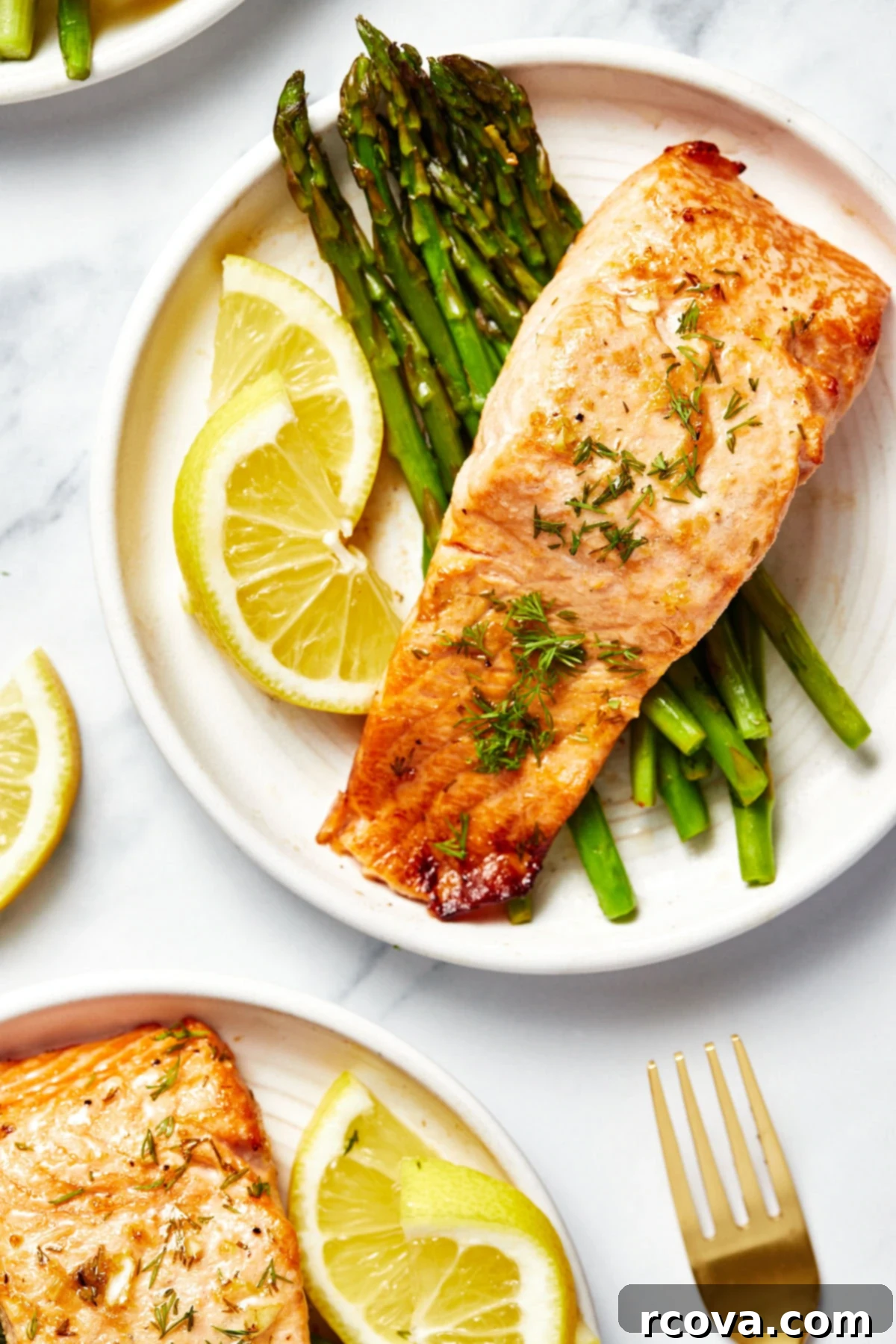 30-Minute Air Fryer Salmon 6 A close-up view of two meticulously plated servings of air fryer salmon, each resting on a bed of vibrant green asparagus and elegantly garnished with thin slices of fresh lemon.